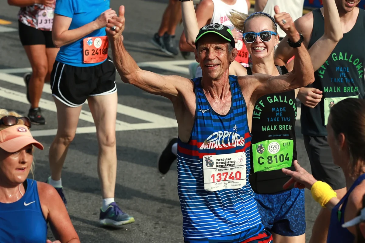 Jeff Galloway gives a double thumbs-up as he heads to the finish line in the 50th AJC Peachtree Road Race in Atlanta in 2019. Galloway won the race in its first year.Curtis Compton / AP file