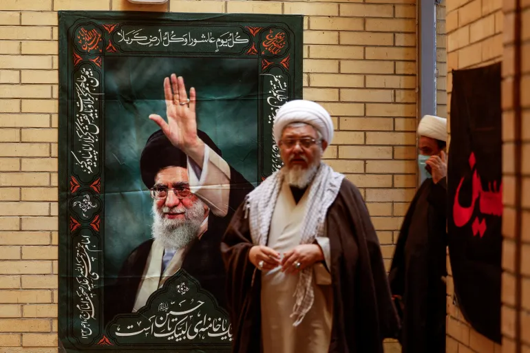 Clerics walk past a wall with a poster of Iran's Supreme Leader Ayatollah Ali Khamenei, after offering their condolences following his killing in Israeli and US strikes, at the office of the supreme leader's representative in Najaf, Iraq, March 1, 2026 [Alaa al Marjani/Reuters]